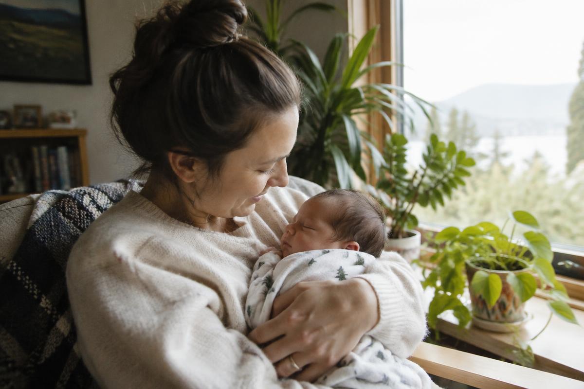 Parent holding a sleeping newborn by a window